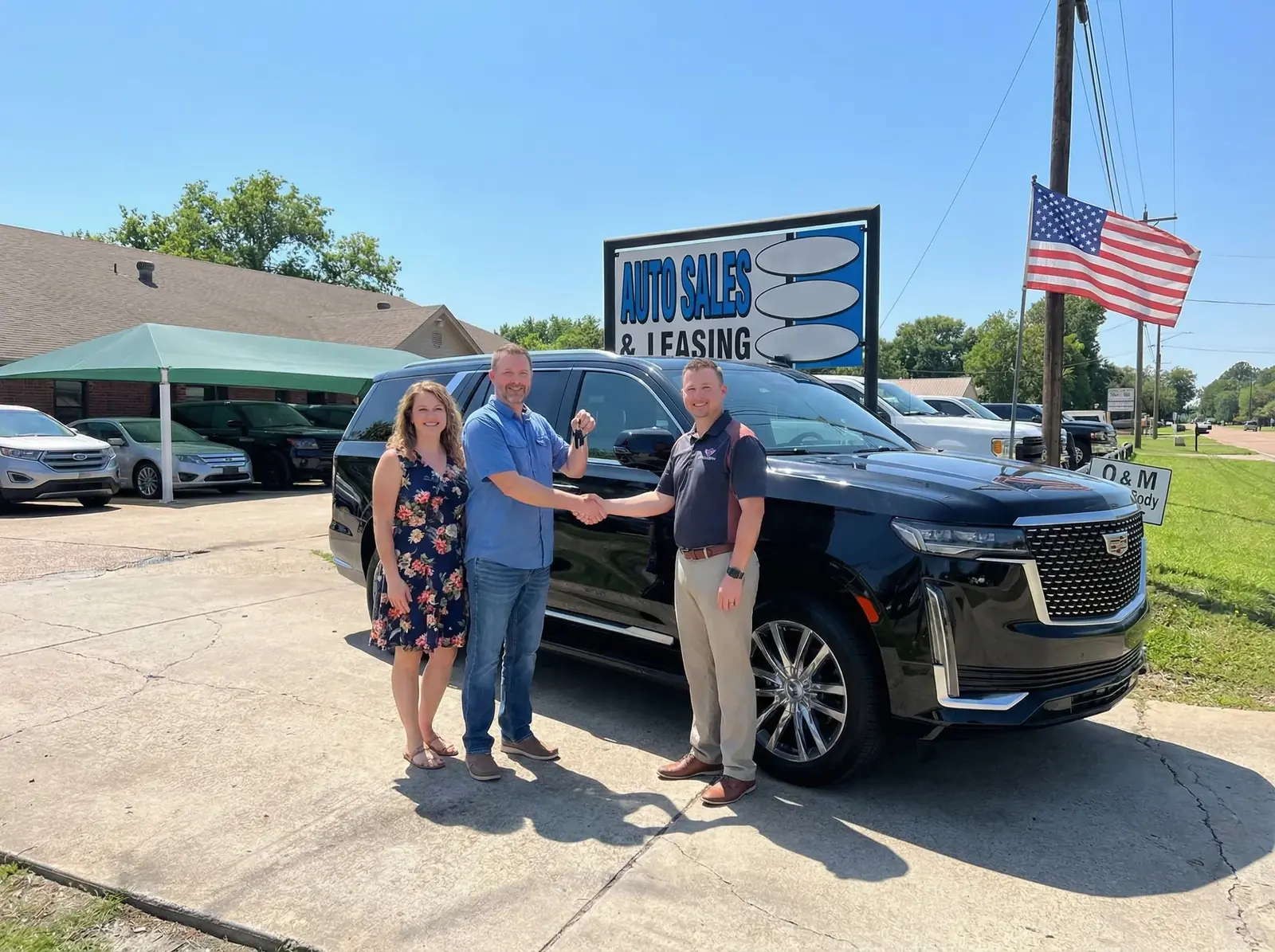 A couple shaking hands with a salesman beside their new SUV on the lot